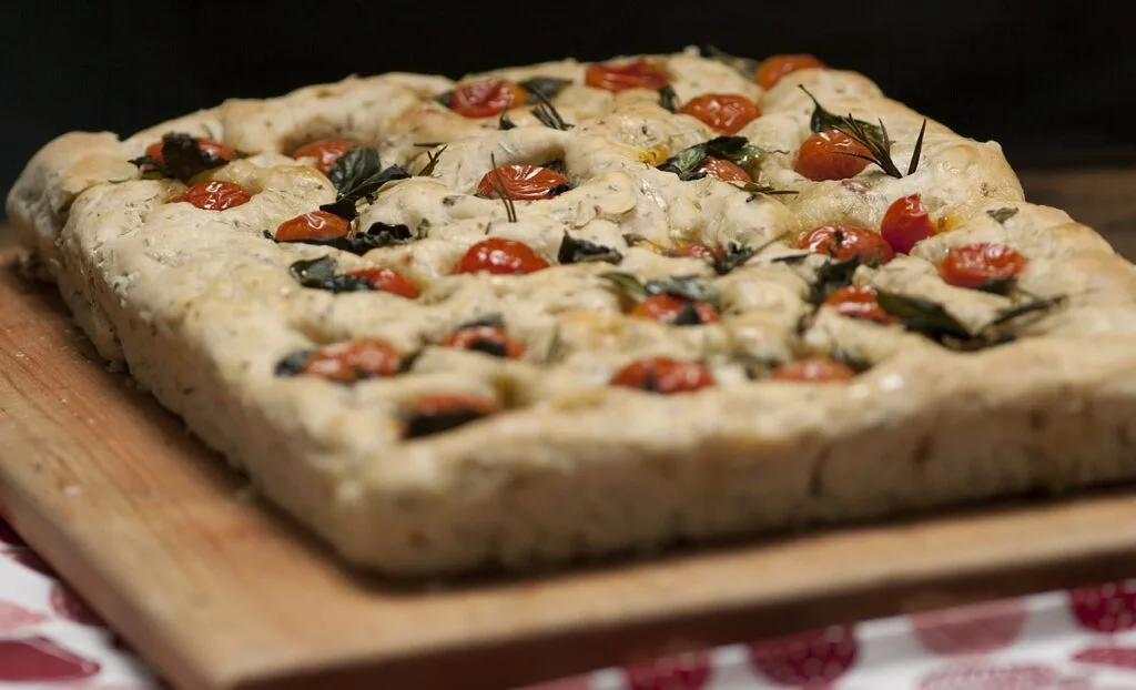 Kwadratowa focaccia z pomidorkami i świeżymi ziołami na desce