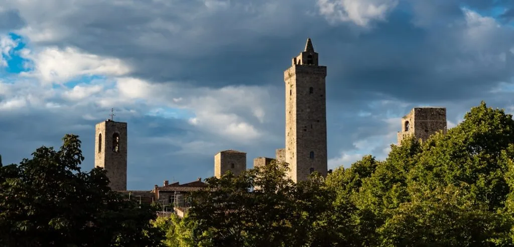 Kamienne średniowieczne wieże San Gimignano ponad zielonymi drzewami