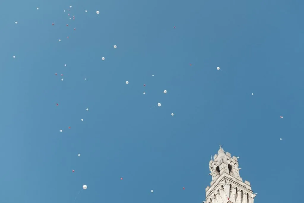 Białe i czerwone balony nad wieżą Torre del Mangia w Sienie